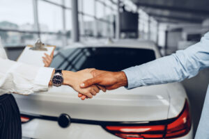 Woman car seller and man car buyer handshaking in car salon building